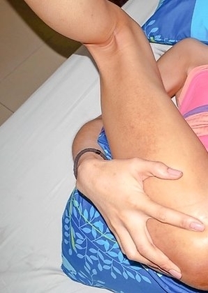 Tall and sexy Ladyboy Swan is sitting on the bed wearing a pink multi-colored blouse, red panties, and flat white sneakers.